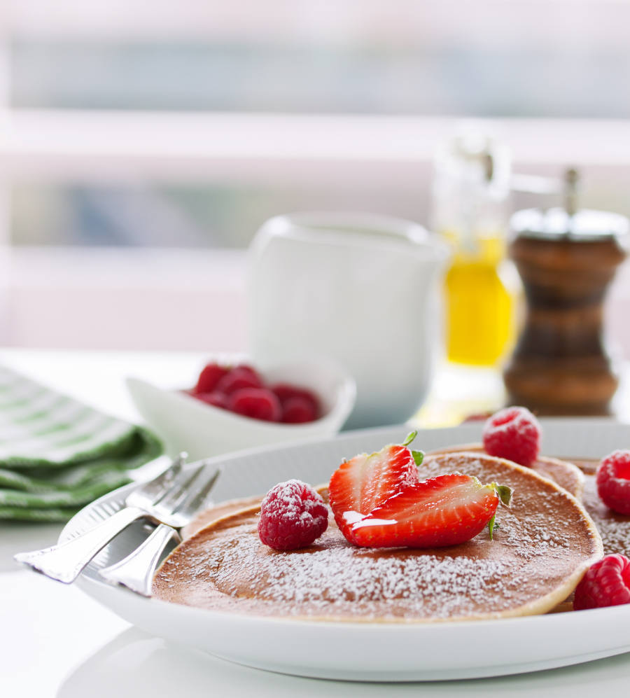 Pancake americani fatti in casa con latticello, fragole e lamponi freschi su un piatto bianco su un tavolo bianco per la colazione, primo piano, messa a fuoco selettiva